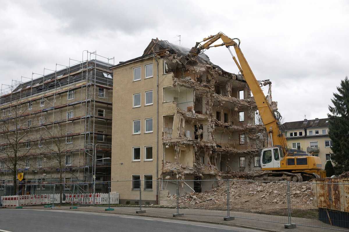 Bagger mit Abbruchgreifer arbeitet an einem Wohngebäude in einer deutschen Straße, Gerüst am Nachbargebäude, Symbolbild.